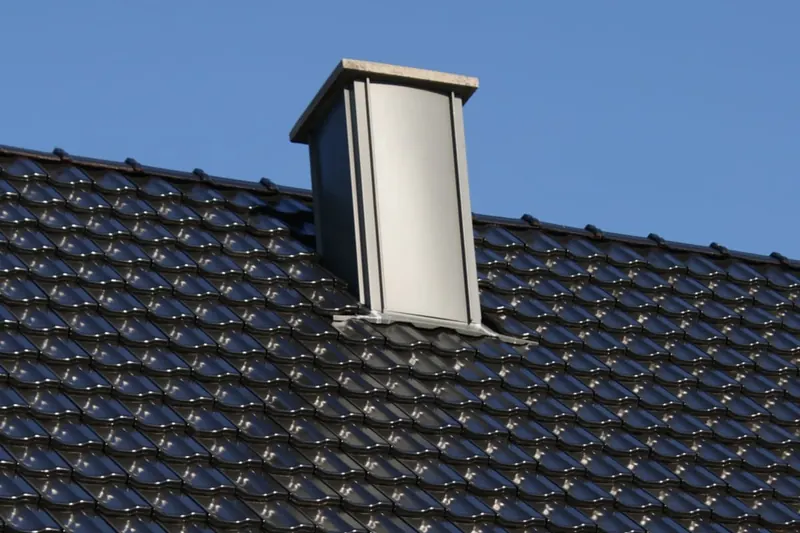 Kaminverkleidung aus Metall auf schwarzem Ziegeldach
